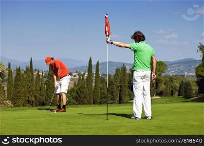 Flight of two golfers playing on the green of a golf course