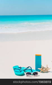 Flip flop, suncream bottles, goggles, starfish and sunglasses on white sand beach background ocean. Suncream bottles, goggles, starfish and sunglasses on white sand beach background ocean