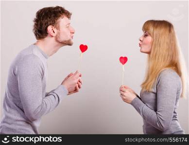 Flirt on date concept. Valentine's Day. Young charming loving pare with love sign symbols little red hearts on sticks. Couple flirting and dating.. Loving pare with hearts flirting.