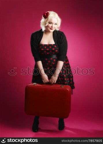Flirting pin-up girl and old retro suitcase and she looks toward the camera, pink background