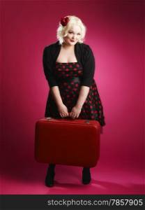 Flirting pin-up girl and old retro suitcase and she looks toward the camera, pink background
