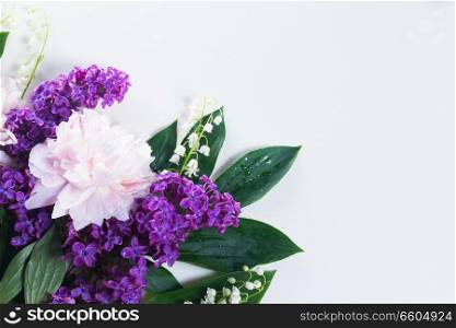 Floral flat lay csene of fresh flowers - lilac, peonies and lilly of the walley flowers on white background. Floral borders