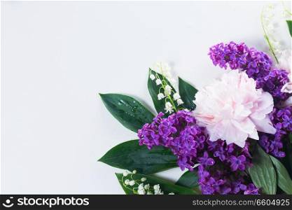 Floral flat lay csene of fresh flowers - lilac, peonies and lilly of the walley flowers on white background. Floral borders