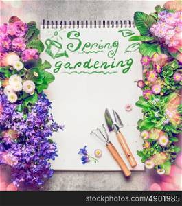 Floral Gardening background with assortment of colorful garden flowers, paper notebook ,gardening tools and text Spring Gardening, top view, frame