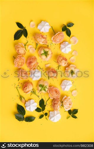Floral pattern with pink roses and merengues on yellow background, flat lay, vertical composition. Food texture, background and wallpaper