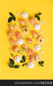 Floral pattern with pink roses and merengues on yellow background, flat lay, vertical composition. Food texture, background and wallpaper