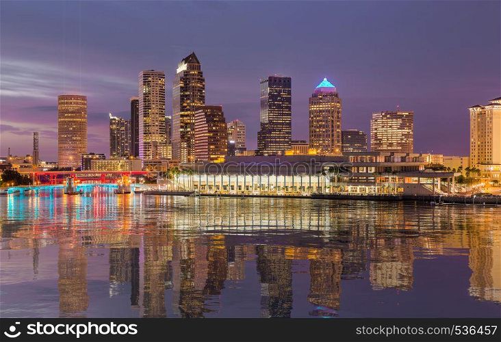 Florida skyline at Tampa with the Convention Center on the riverbank. Lights are reflected in a smooth artificial water surface. City skyline of Tampa Florida at sunset