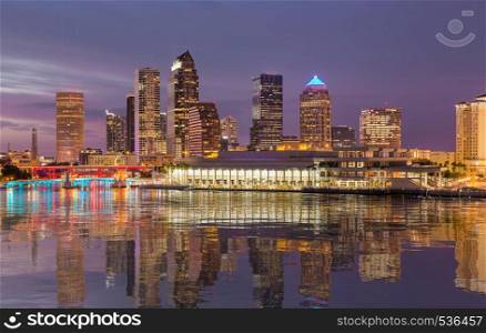 Florida skyline at Tampa with the Convention Center on the riverbank. Lights are reflected in a smooth artificial water surface. City skyline of Tampa Florida at sunset