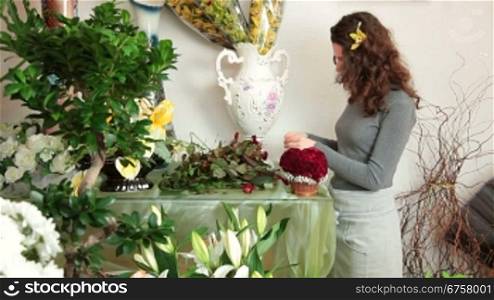 Florist arranging rose heart-shaped bouquet is surrounded by gypsophila in flower shop. Medium shot