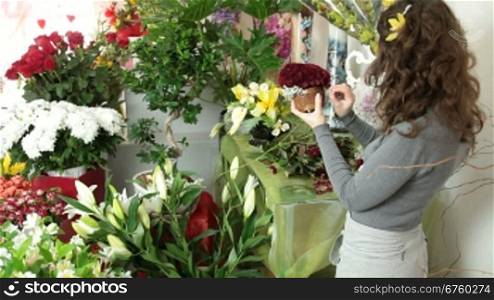 Florist arranging rose heart-shaped bouquet is surrounded by gypsophila in flower shop. Medium shot