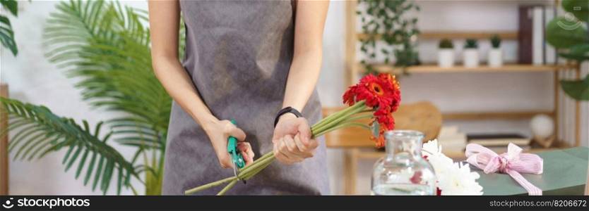 Florist concept, Female florist cutting stems of red gerbera with scissor for making flower bouquet.