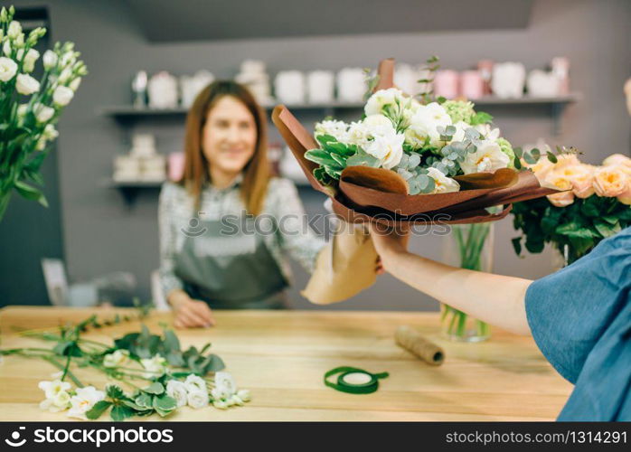 Florist gives fresh bouquet to female customer in flower boutique. Floral shop interior on background. Florist gives fresh bouquet to female customer