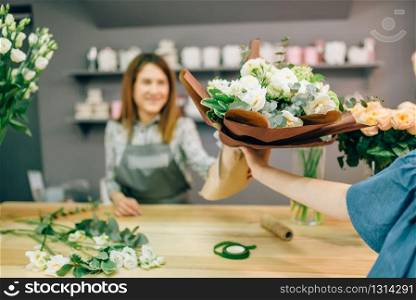 Florist gives fresh bouquet to female customer in flower boutique. Floral shop interior on background. Florist gives fresh bouquet to female customer