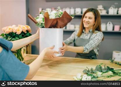 Florist gives fresh flower composition in vase to female customer in flower boutique. Floral shop interior on background