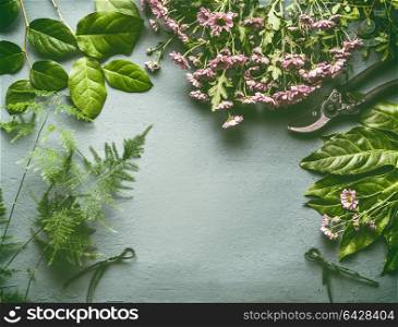 Florist work space with a lot of fresh green leaves , pink flowers and shears, flat lay, frame with copy space for your design