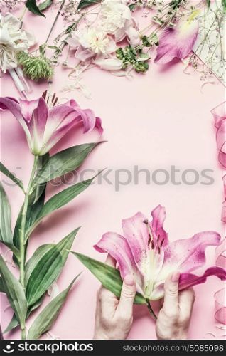 Florist workspace. Female hands holding beautiful pink lily flowers on pastel table with florist decoration equipment, top view, frame. Creative Flowers arrangement. Invitation and holiday, concept