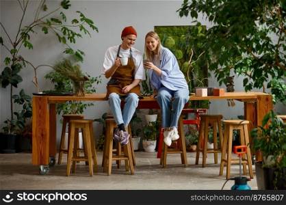 Floristic workshop. Professional floral artist talking and smiling sitting on table at decoration shop. Professional floral artist talking and smiling sitting on table