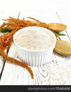Flour amaranth in a bowl, a spoon with grain, brown flower with green leaves on the background light wooden boards