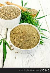 Flour and hemp grain in white bowl and spoon, cannabis leaves on the background of wooden boards