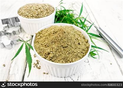 Flour and hemp grain in white bowls, mixer and cookie cutters, cannabis leaves on the background of light wooden boards