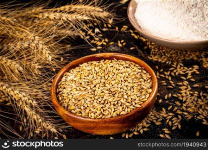 Flour and rye grains in bowls. On a black background.. Flour and rye grains in bowls.