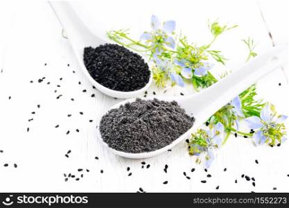 Flour and seeds of Nigella sativa in two spoons, sprigs of kalingini with blue flowers and green leaves on a light wooden board background