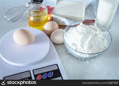 Flour and sugar in a glass container, eggs and butter on a white table. Ingredients for cooking.. Ingredients for cooking. Flour and sugar in a glass container, eggs and butter on a white table.