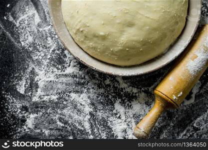 Flour background. The dough in a bowl with a rolling pin. On rustic background. Flour background. The dough in a bowl with a rolling pin.