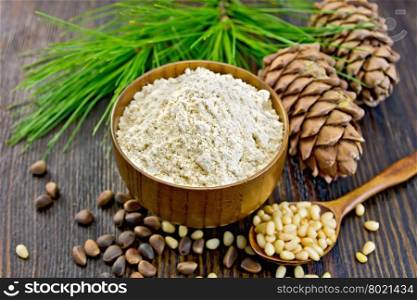 Flour cedar in a wooden bowl, cedar nuts and two cones, a spoon with peeled nuts, cedar branch against the dark wooden board