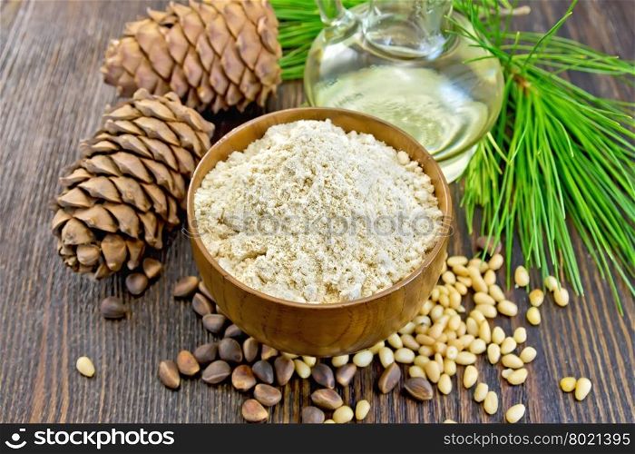Flour cedar in a wooden bowl, cedar nuts and two cones, the oil in the glass carafe, cedar branch against the backdrop of wooden planks