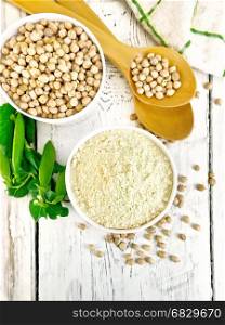 Flour chickpeas and chick-pea in white bowls and spoons, pods of green beans on the background of the wooden planks on top