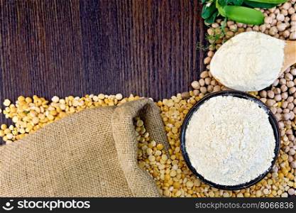 Flour chickpeas in a bowl and of pea in a spoon, green pods on burlap background on wooden board