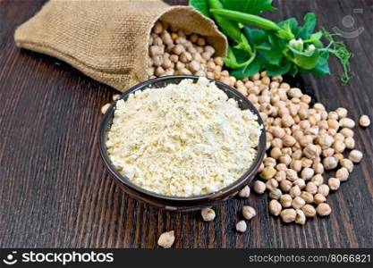 Flour chickpeas in a bowl, chick-peas in a sack and fresh pea pods on a background of dark wood planks