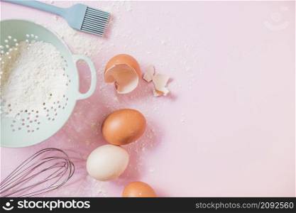 flour colander eggs whisk against pink background