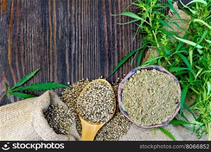 Flour in a bowl and hemp seeds in a spoon, green twigs of cannabis on sackcloth background on wooden board