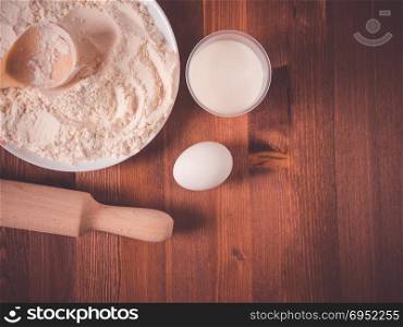 Flour in a bowl, white eggs and a wooden rolling pin on a wooden background. Top view