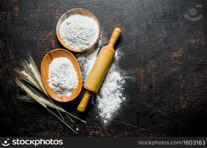 Flour in bowls with spikelets and a rolling pin. On dark rustic background. Flour in bowls with spikelets and a rolling pin.