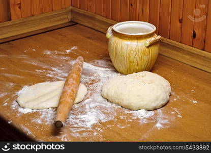 Flour in capacity with dough and rolling pin on the wooden table