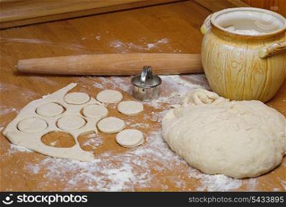 Flour in capacity with dough and rolling pin on the wooden table