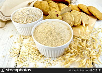 Flour oat and bran in white bowls, oatmeal and stems, bread and biscuits, napkin on a background of wooden boards
