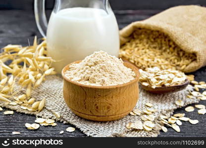 Flour oat in a bowl, milk in a jug, oatmeal in a spoon on burlap, grain in bag, oaten stalks on wooden board background