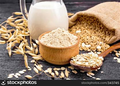 Flour oat in a bowl, oatmeal in a spoon, grain in a bag, oaten stalks on the background of dark wooden board