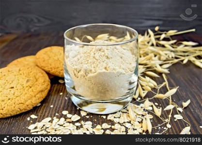 Flour oat in a glassful, oatmeal and ears, cookies on a background of wooden boards