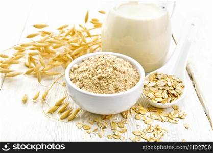 Flour oat in bowl, milk in a jug, oatmeal in spoon, oaten stalks on the background of light wooden board