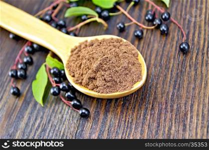 Flour of bird-cherry in a spoon with berries on a background of wooden boards