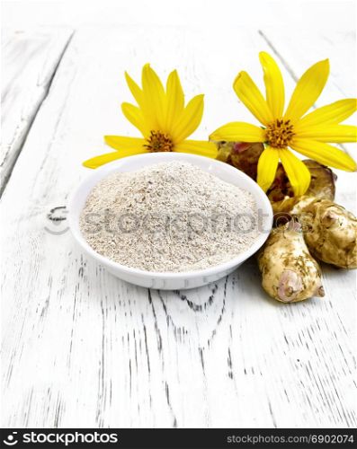 Flour of Jerusalem artichoke in a white bowl with flowers and vegetables on the background of wooden boards