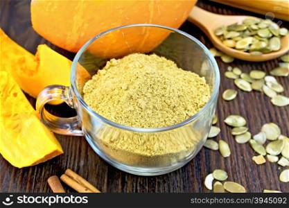 Flour pumpkin in a glass cup, rolling pin, spoon and cinnamon, fresh pumpkin, pumpkin seeds on the background of dark wooden board