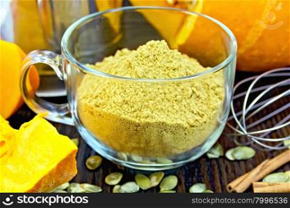 Flour pumpkin in a glass cup, sieve, mixer and cinnamon, cloves fresh pumpkin, pumpkin seeds on the background of dark wooden board