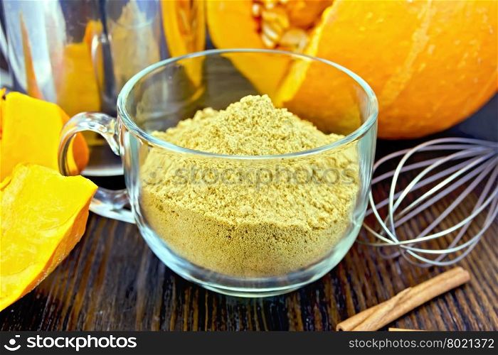 Flour pumpkin in a glass cup, sieve, mixer and cinnamon, cloves fresh pumpkin on a wooden boards background