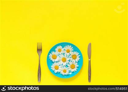 Flower chamomile daisy on blue plate and cutlery fork knife on yellow paper background Concept vegetarianism, healthy eating or diet Creative top view Copy space template for lettering text or your design.. Flower chamomile daisy on blue plate, cutlery fork knife on yellow paper background Concept vegetarianism, healthy eating or diet Creative top view Copy space template for lettering text or design